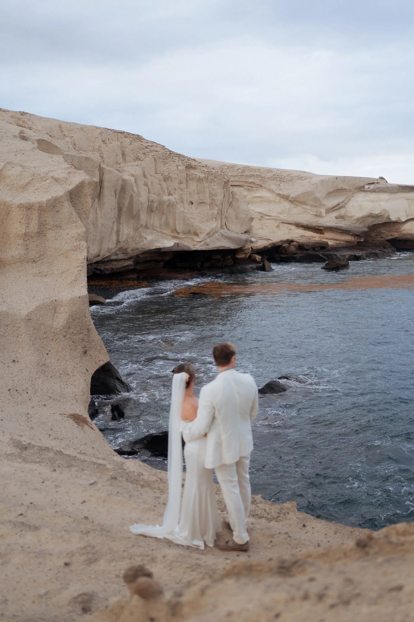 Couple standing together on pale coastal rocks above the sea