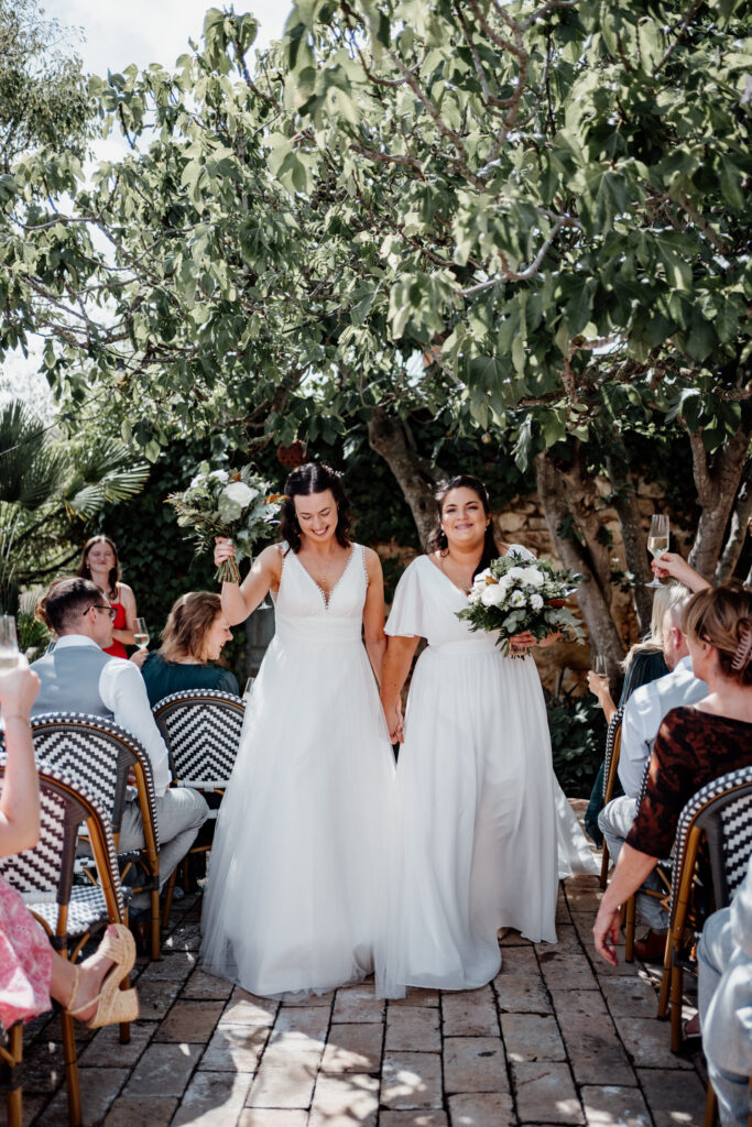 Newlyweds walking down the outdoor aisle with bouquets