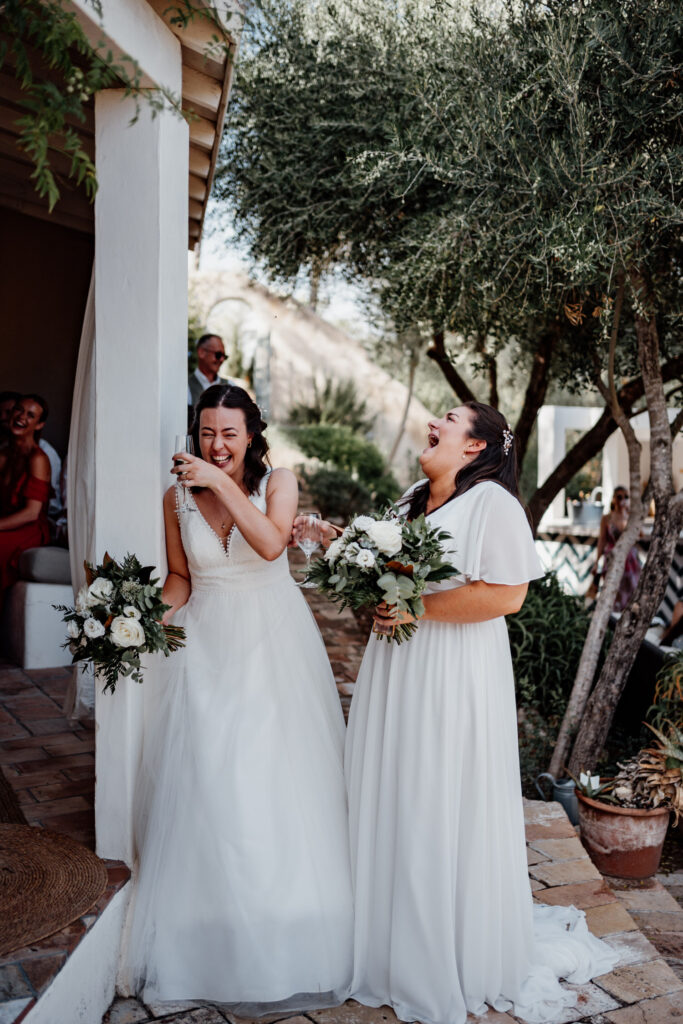 Bride wiping her face as her partner laughs beside her