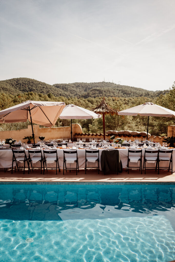 Long reception tables beside a swimming pool with hills beyond