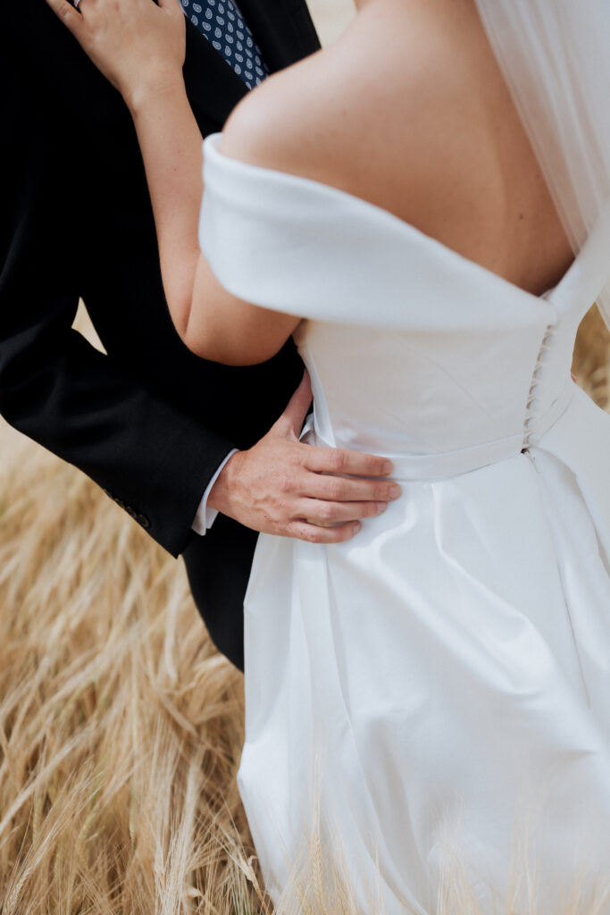 Close-up of the groom's hand at the bride's waist in the field