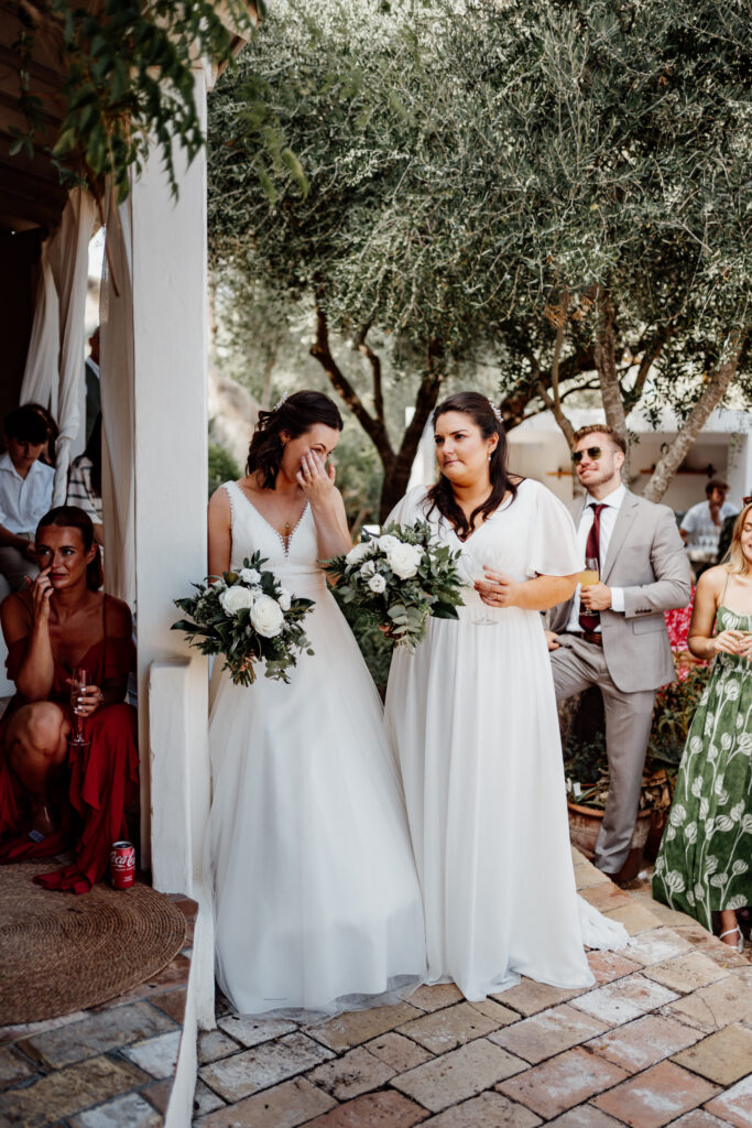 Bride wiping away tears beside her partner outside the villa