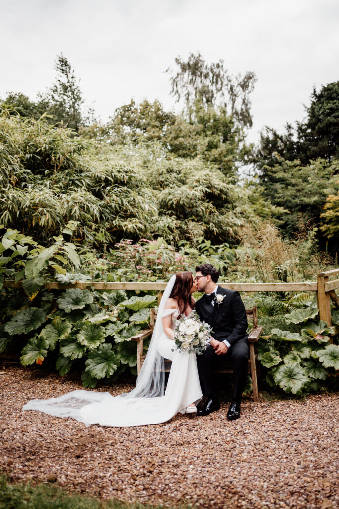 Bride and groom kissing while seated on a garden bench