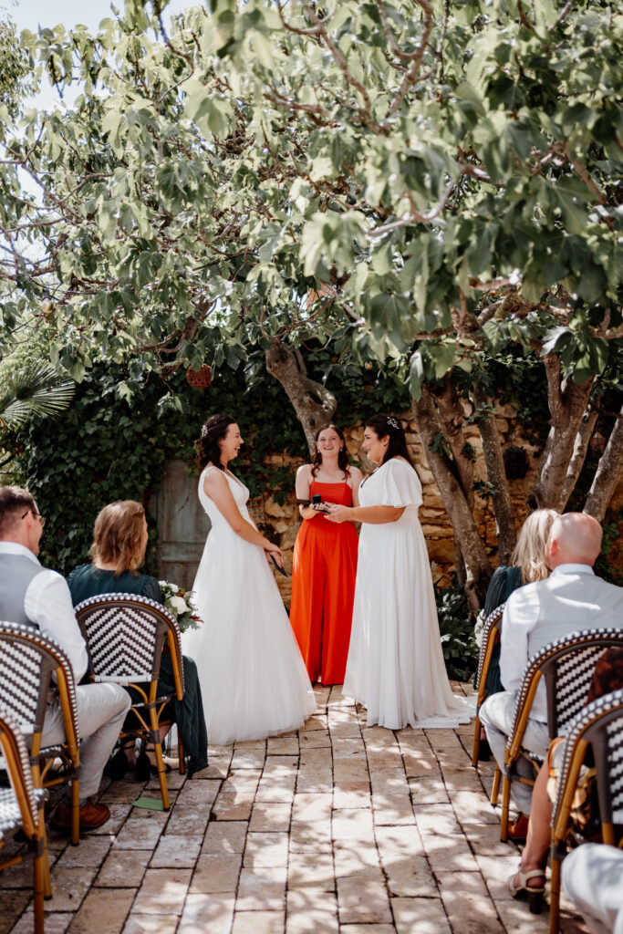 Wedding celebrant standing with two brides under a leafy tree