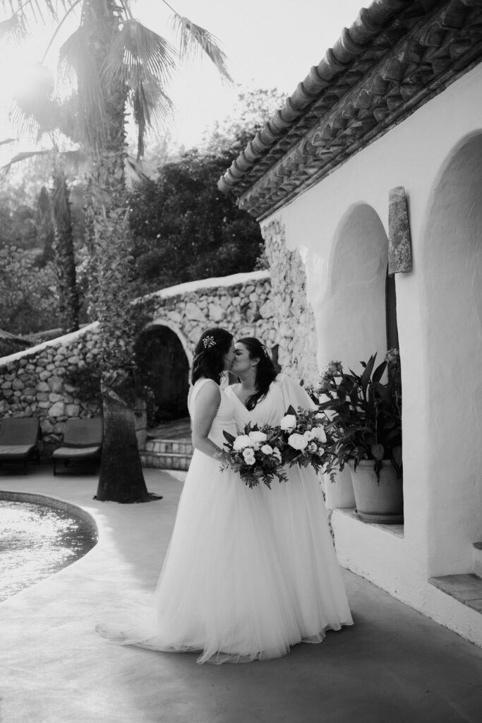 Black-and-white portrait of newlyweds beside the pool and villa arches