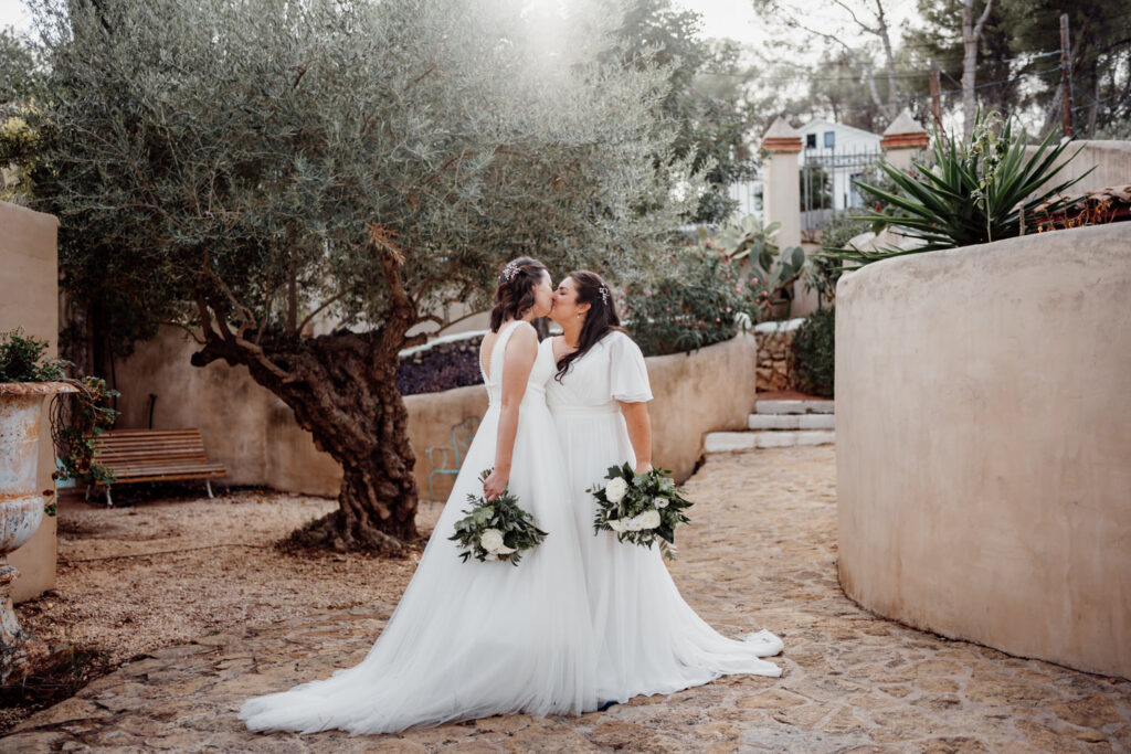 Newlyweds kissing beside olive trees in a sunlit courtyard