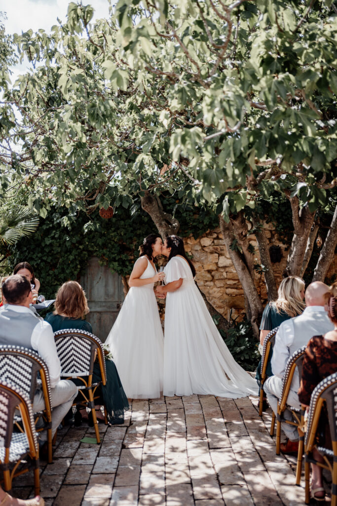 Two brides exchanging vows beneath a leafy tree
