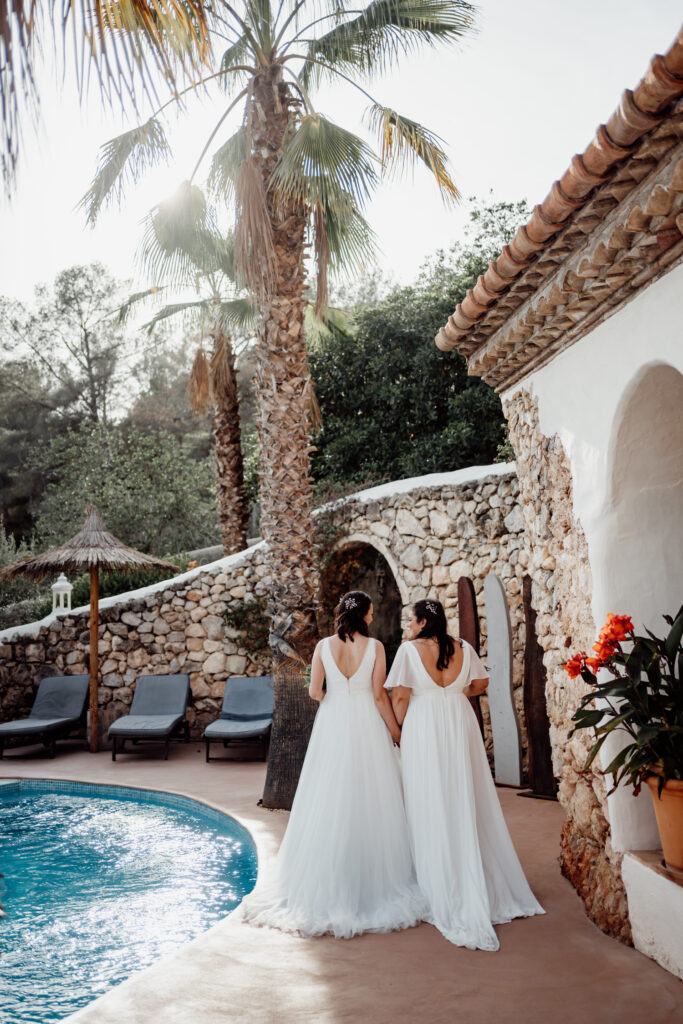 Two brides standing beside the swimming pool beneath a palm tree