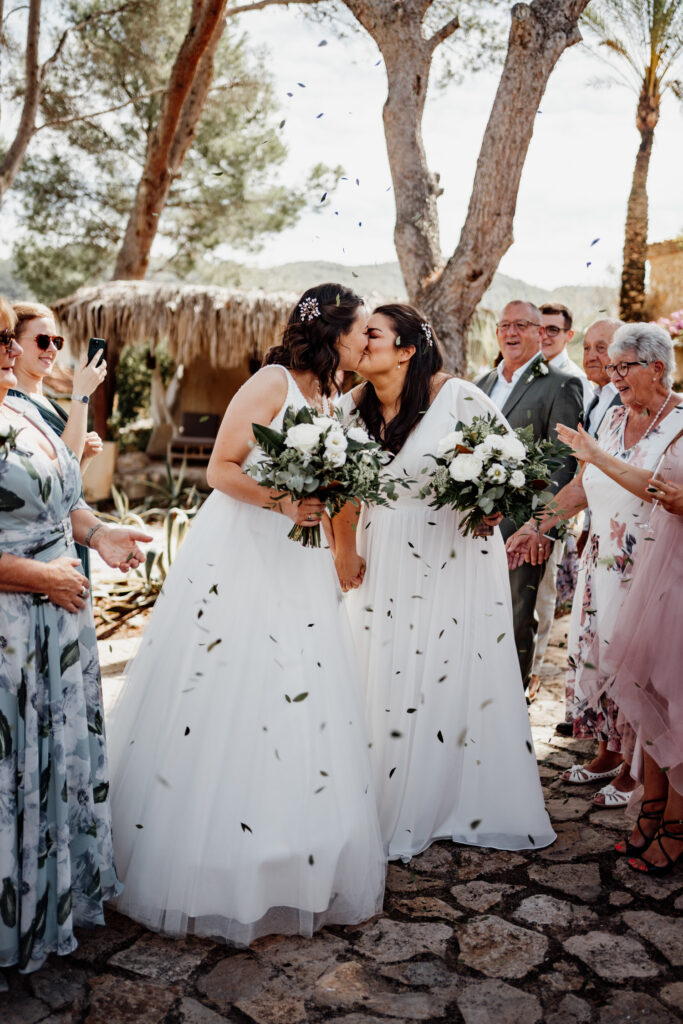 Newlyweds kissing while guests throw confetti on the garden path