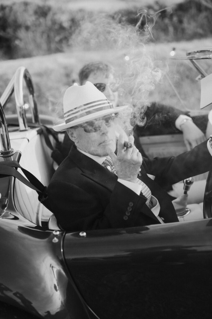 Wedding guest smokes a cigar whilst say in the driver seat of a classic car