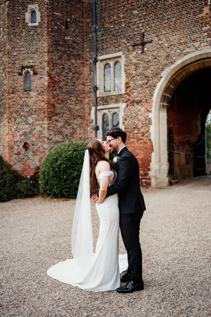 Couple kissing in front of Hodsock Priory's historic brick gatehouse