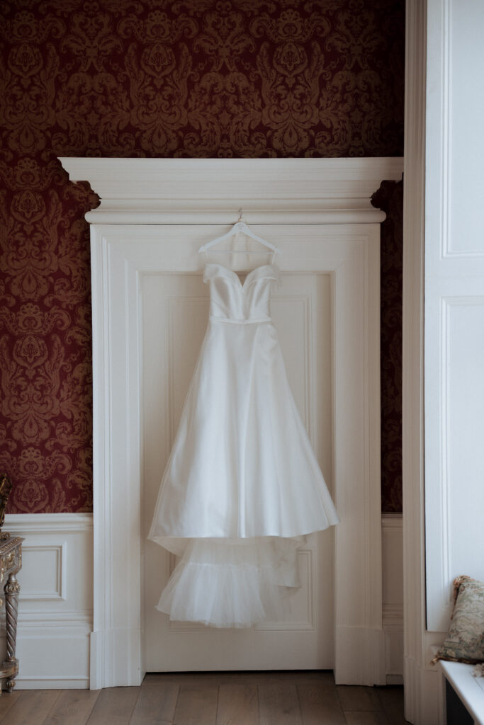 Wedding dress hanging against white panelling in a red-walled room
