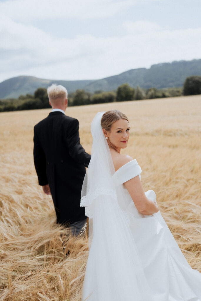 Bride looking back while holding the groom's hand in a golden field