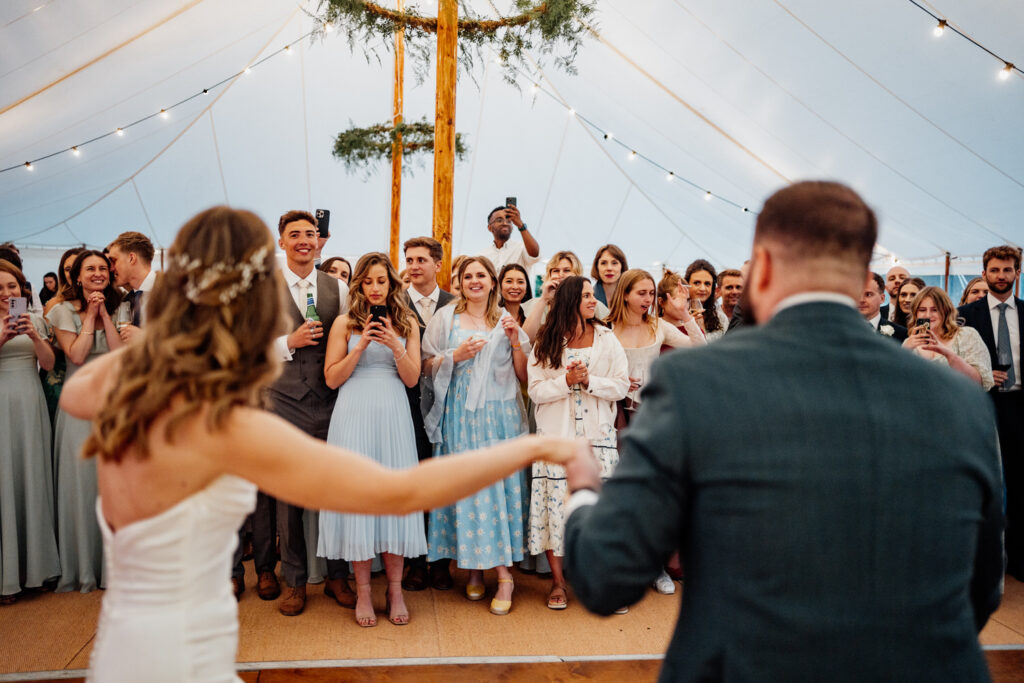 Bride reaching for the groom's hand as guests watch in the marquee