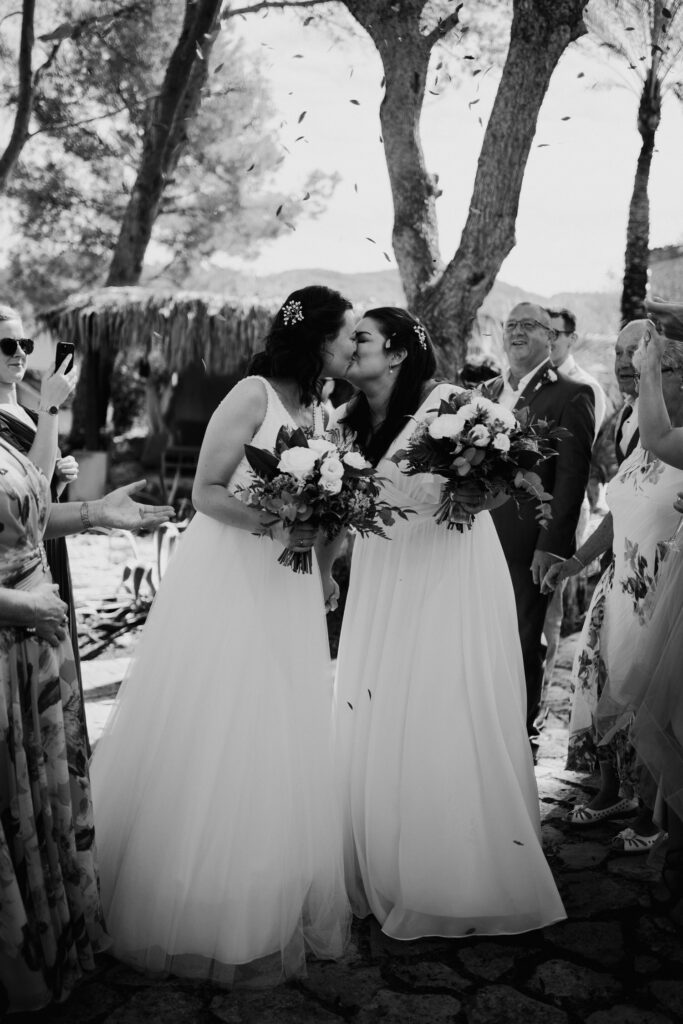 Black-and-white photograph of two brides kissing amid confetti