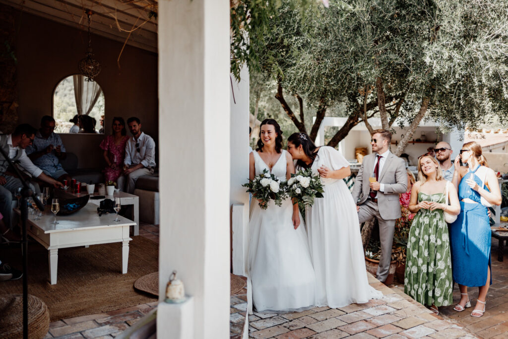 Two brides and guests gathered at the villa entrance
