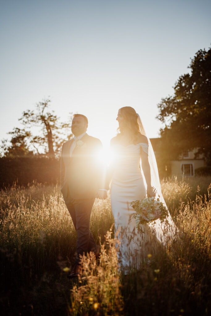 Couple walking through long grass with low sunlight between them