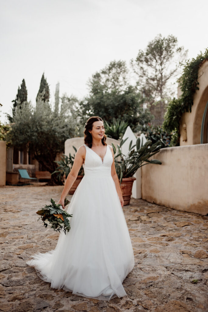 Bride standing with a bouquet on the sunlit courtyard paving