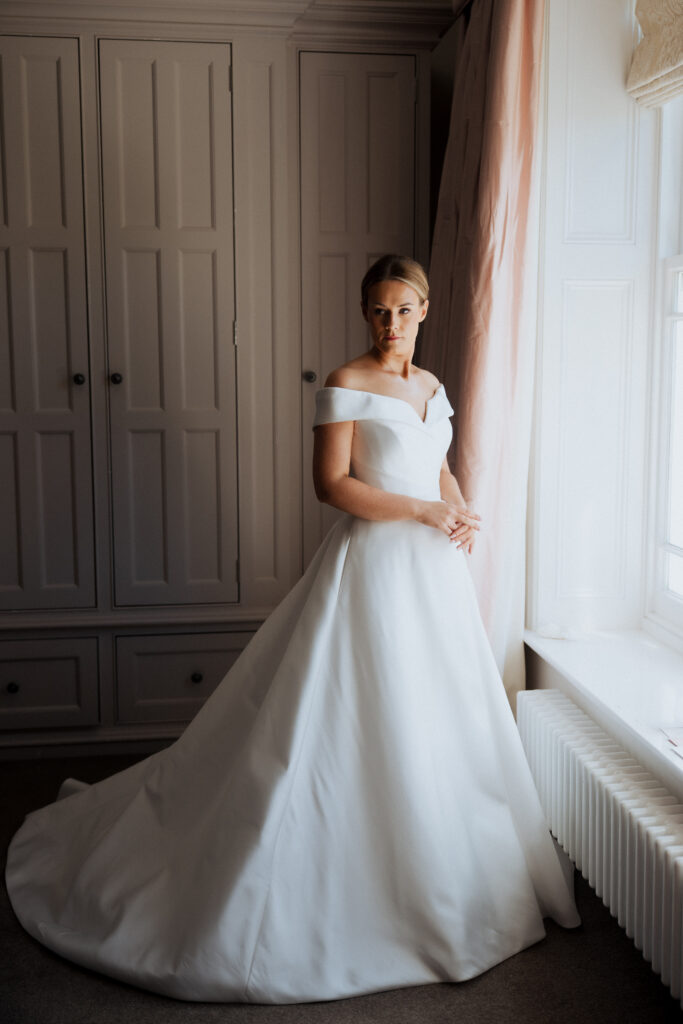Bride standing beside a window with her full skirt spread around her