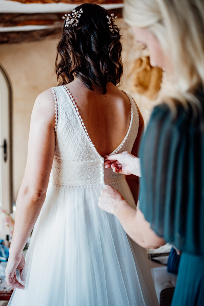 A friend fastening the back of the bride's wedding dress