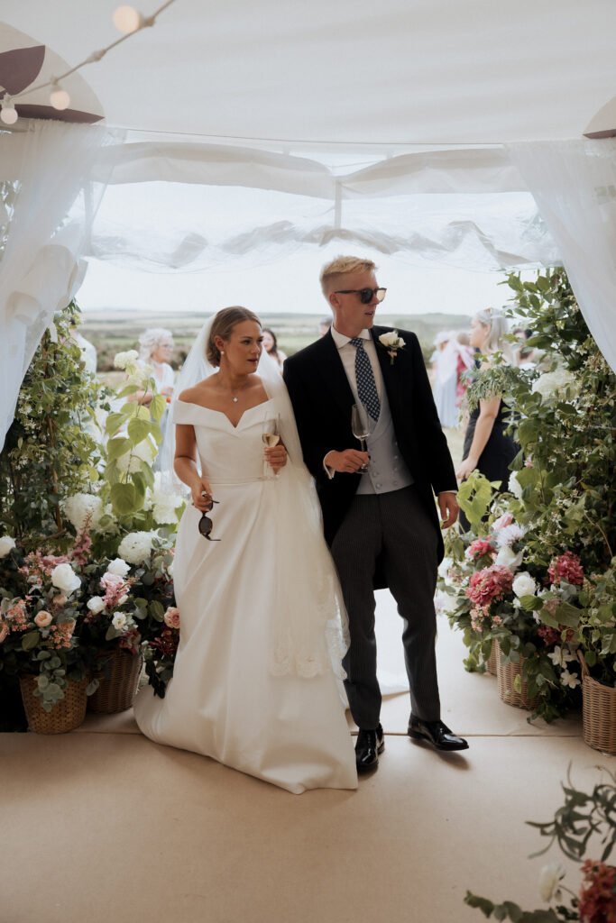 Bride and groom entering their flower-filled reception marquee