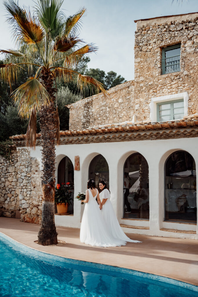 Newlyweds beside the pool with the stone villa and palms behind them