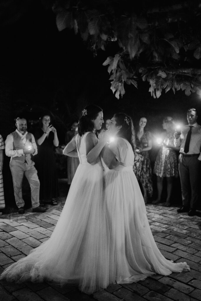 Black-and-white photograph of two brides dancing as guests watch