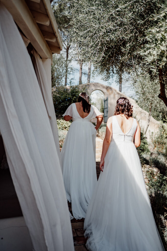 Two brides walking away along a sunlit path
