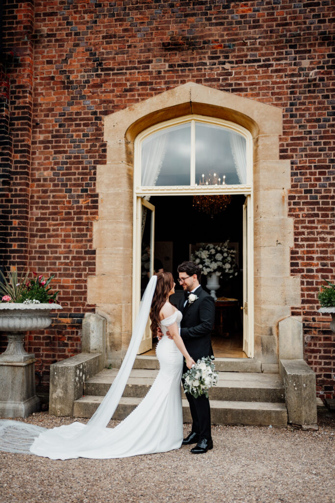 Newlyweds kissing outside a brick doorway with the bride's veil trailing behind