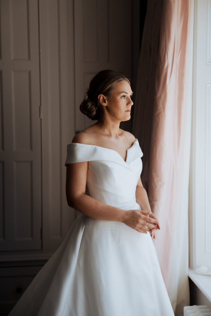 Bride in wedding dress looking out of a window