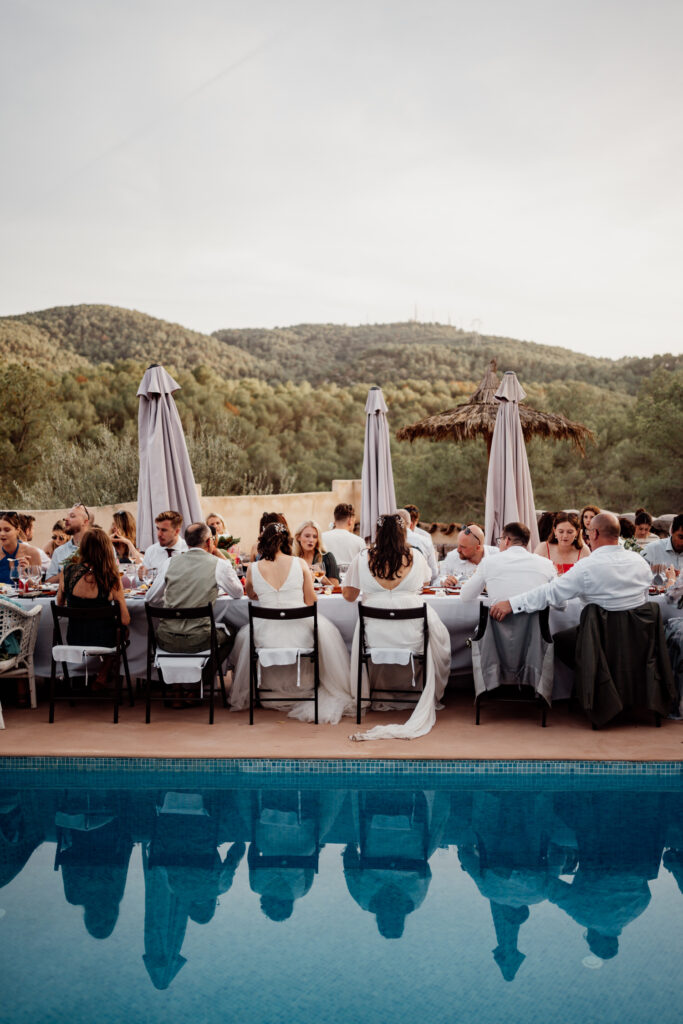 Guests dining beside the pool with wooded hills in the distance