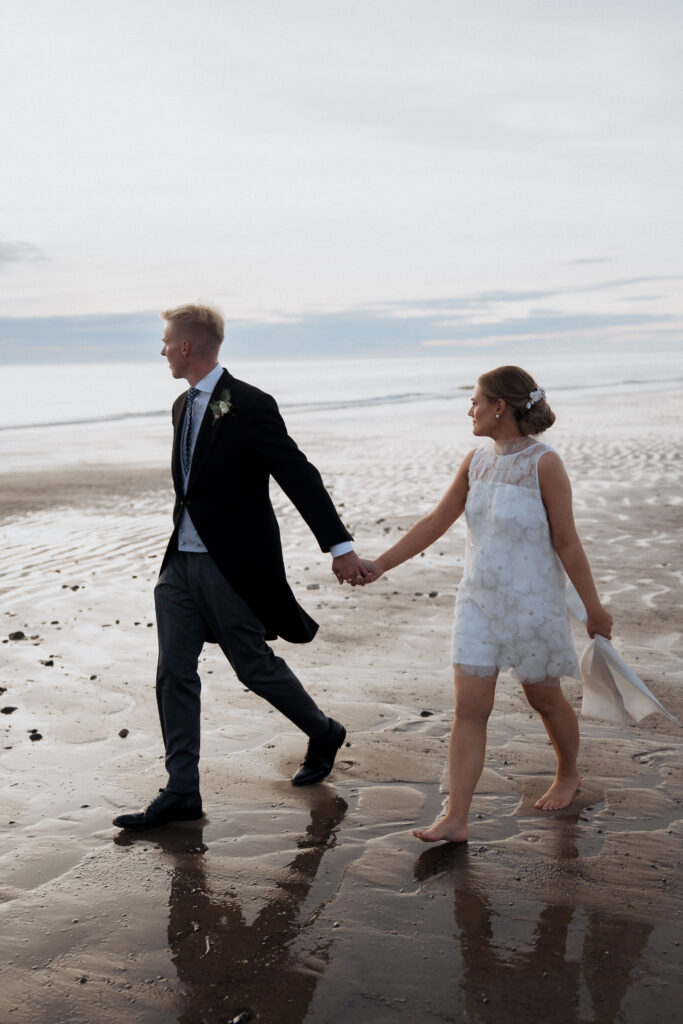 Couple walking hand in hand beside the sea with reflections in the wet sand