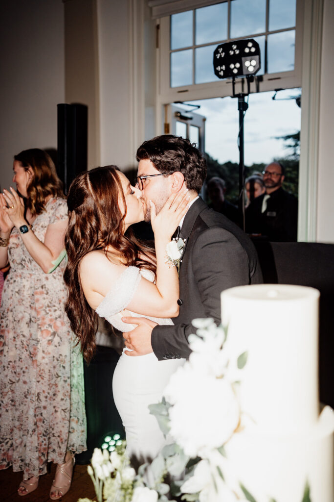 Bride and groom kissing beside their wedding cake at the reception