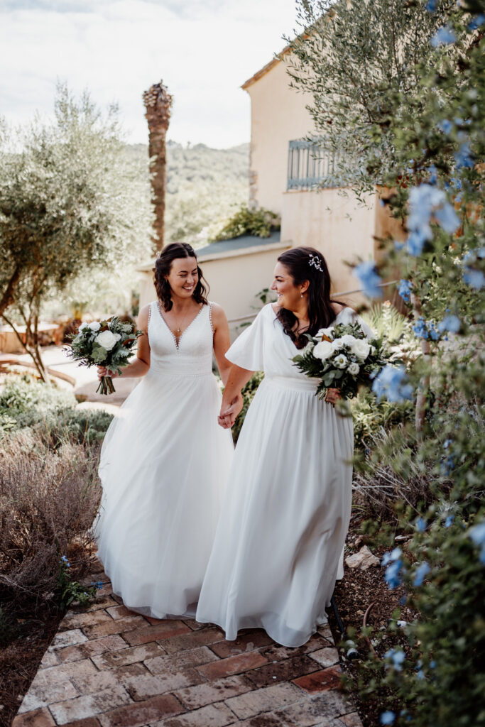 Two brides laughing as they walk through the villa gardens