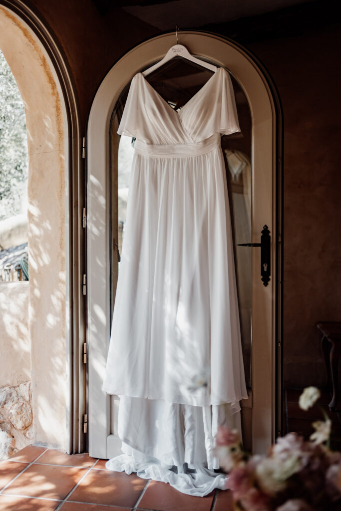 White wedding dress hanging beside an arched window