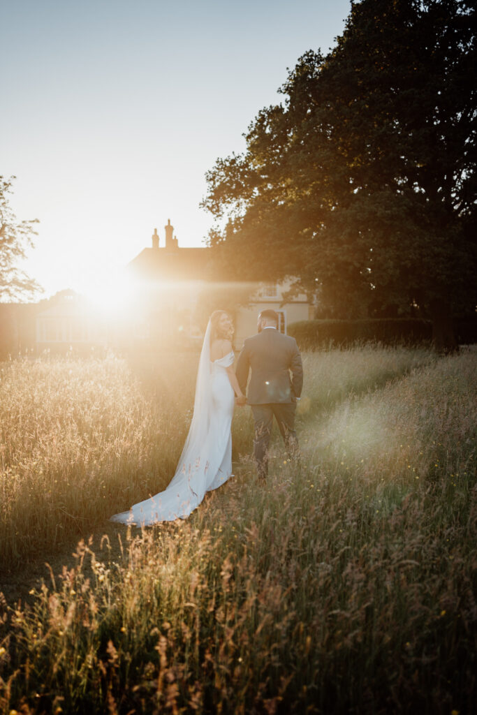 Couple kissing in long grass with the bride's veil lit by the setting sun