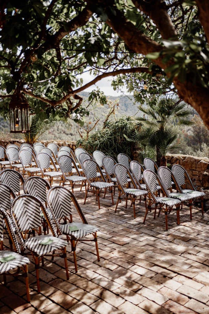 Empty ceremony chairs arranged on a stone terrace beneath trees