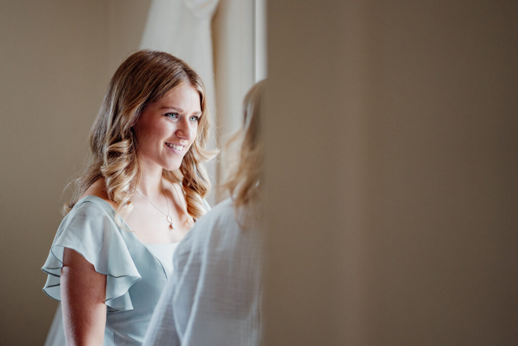 Bride smiling in soft window light while getting ready