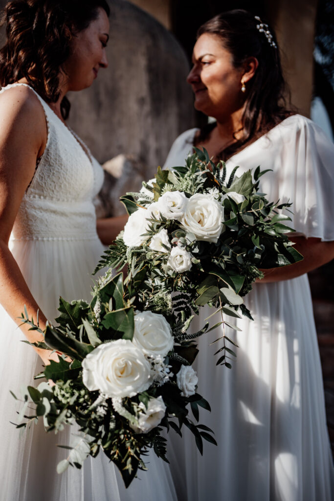 Close-up of two brides with white roses and greenery in their bouquets