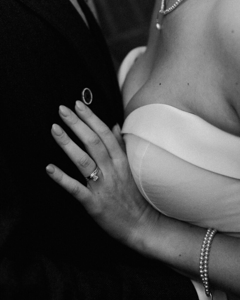 Black-and-white close-up of the bride's wedding ring against the groom's jacket