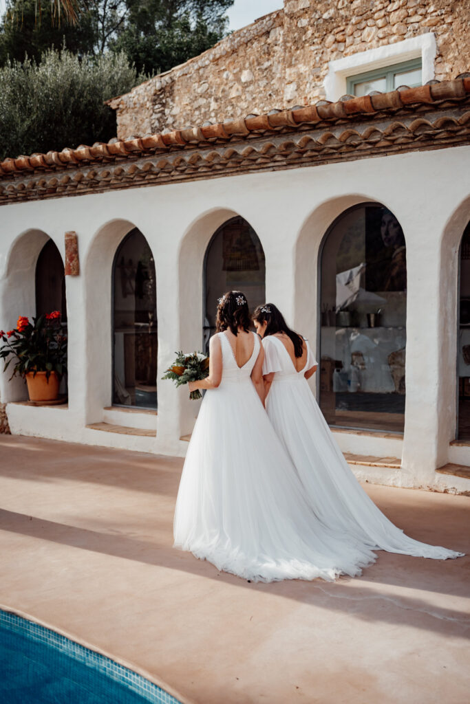 Two brides embracing in front of the villa's arched colonnade