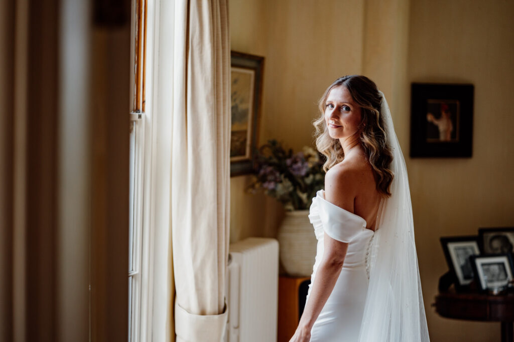 Bride looking over her shoulder beside a bedroom window