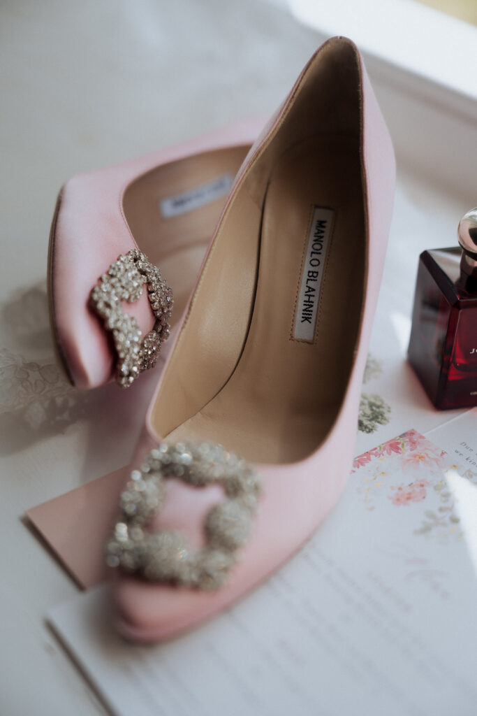 Pink bridal shoes with jewelled buckles beside wedding stationery