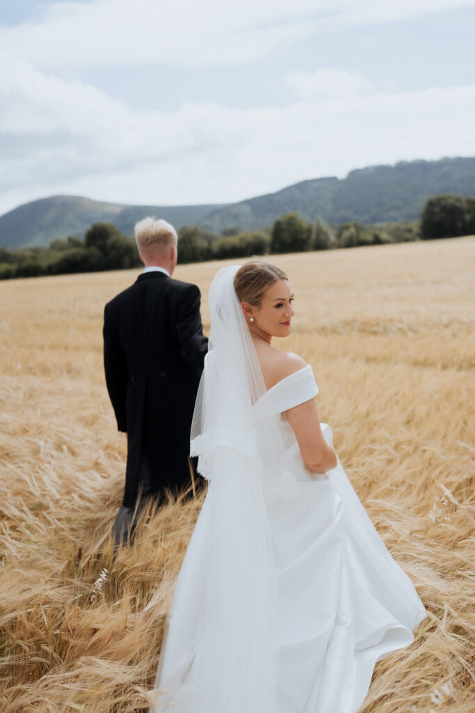 Newlyweds walking away through the field with hills in the distance