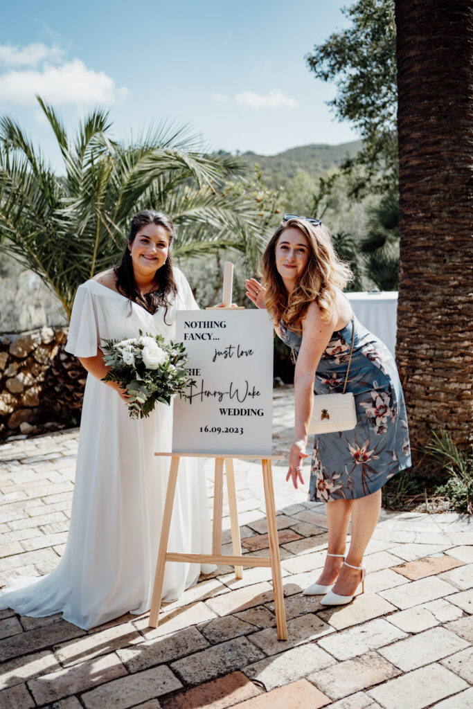 Two guests posing beside the wedding welcome sign