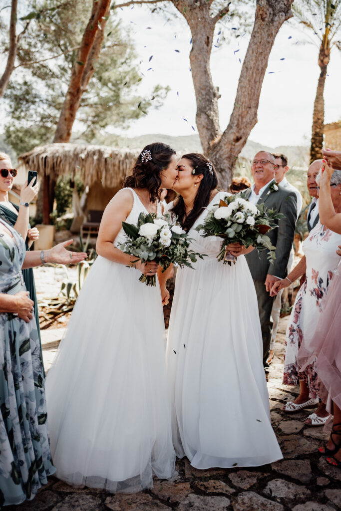Two brides kissing as confetti falls around their bouquets
