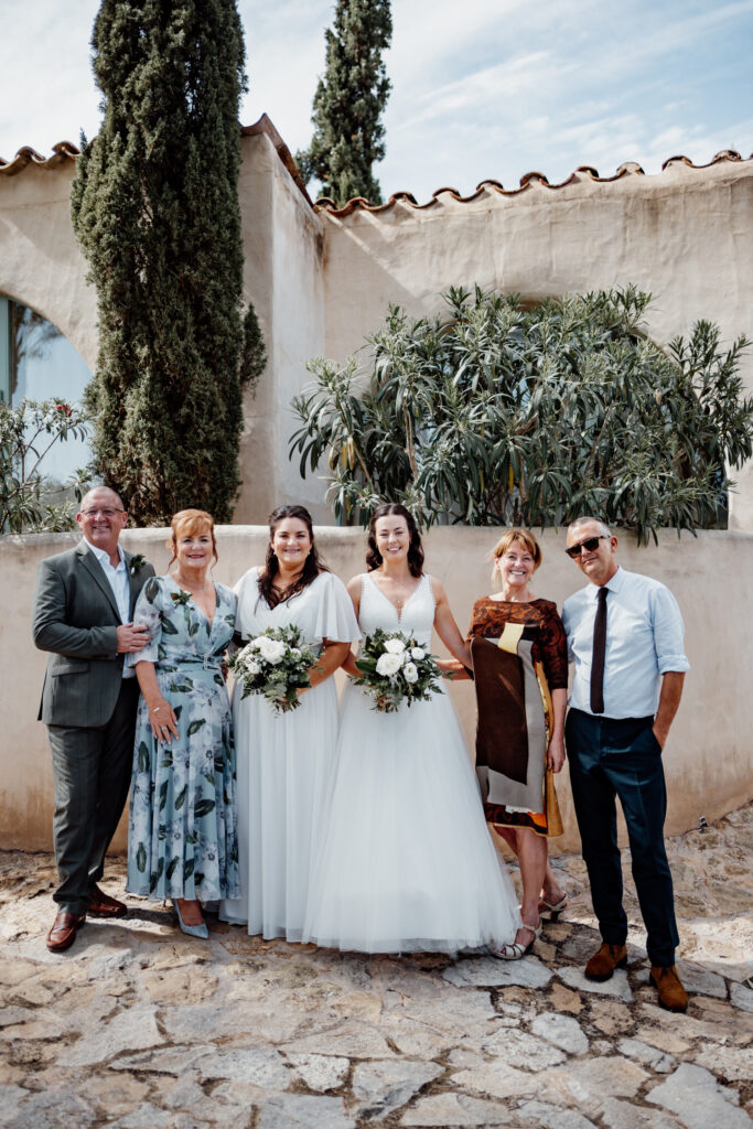 Two brides posing with family on a stone terrace