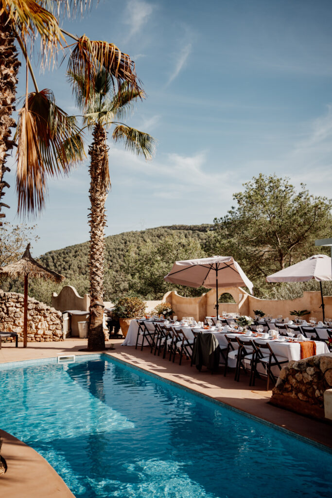 Sunlit pool and wedding reception tables beneath a tall palm