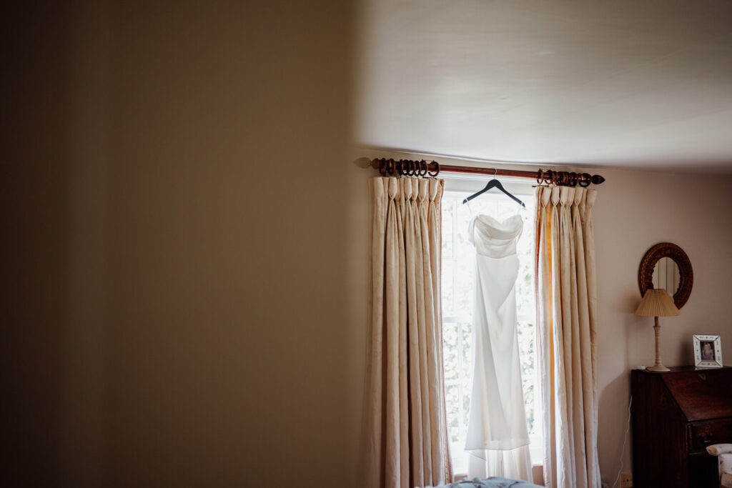 Wedding dress hanging in front of a curtained window