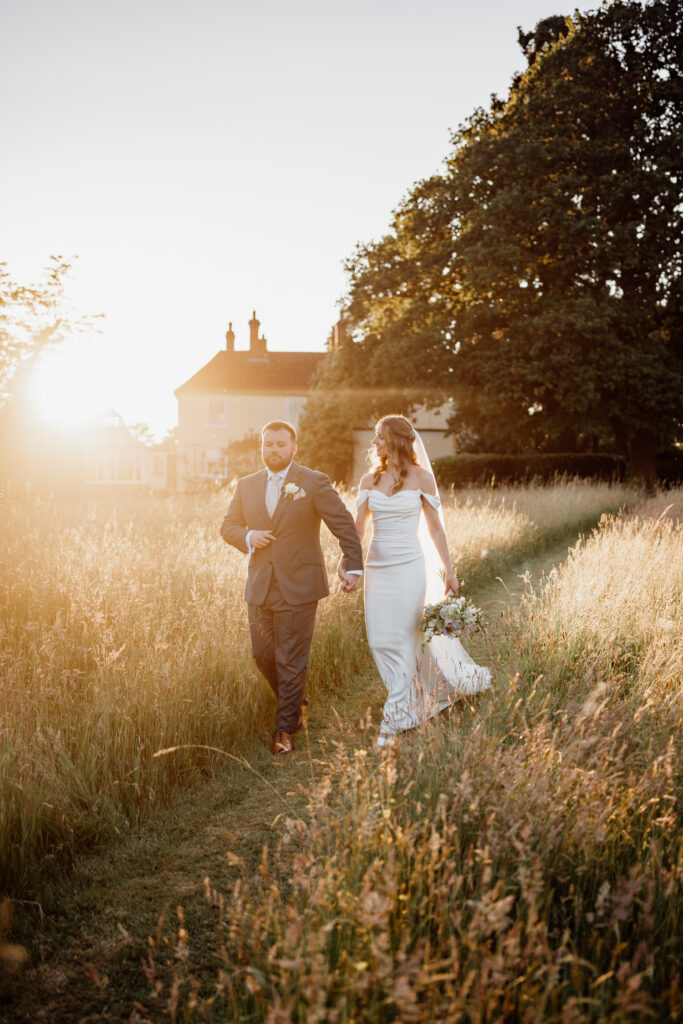 Newlyweds walking towards the camera through a sunlit meadow